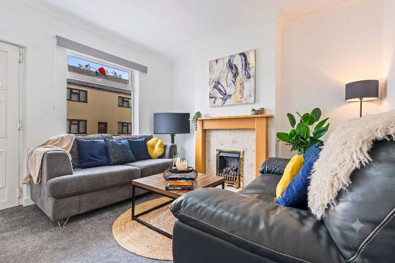 Living room with grey sofa, black leather armchair, fireplace, and city view from window