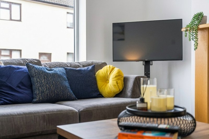 Modern living room with gray sofa, blue and yellow cushions, wall-mounted TV and coffee table