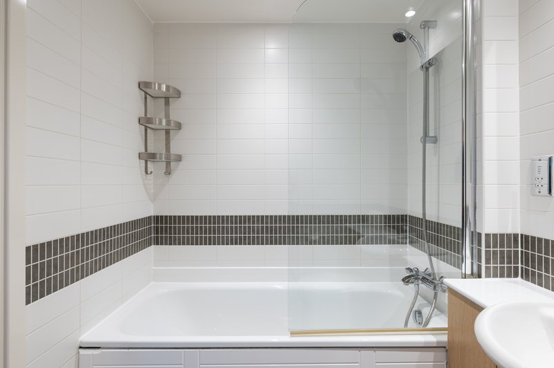 Modern bathroom with white subway tiles, dark stripe accent, bathtub and shower enclosure