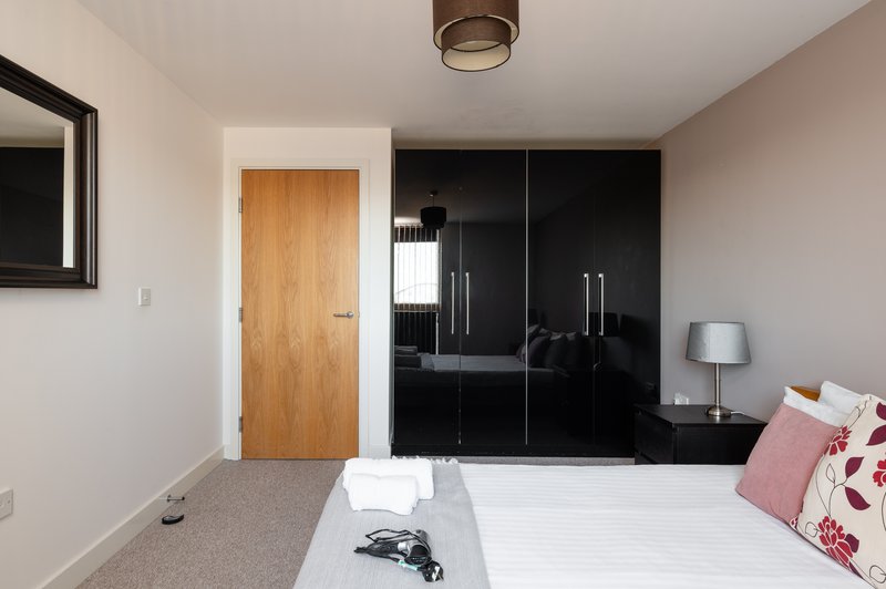 Modern bedroom with double bed, black wardrobe, wooden door and ceiling light