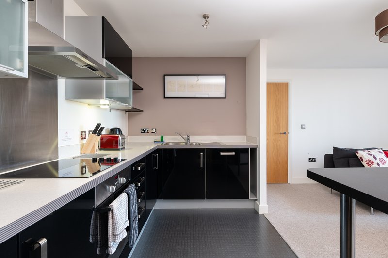 Modern open-plan kitchen and living area with black cabinetry, white countertops, and bed visible in background
