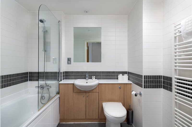 Modern bathroom with white tiles, wooden vanity, round sink and glass shower enclosure