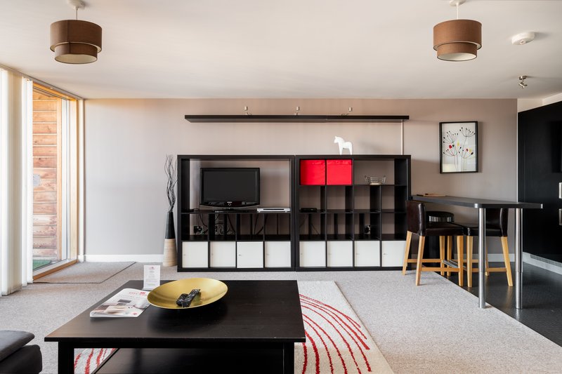 Open-plan living room with black storage unit, TV, dining area, and large windows