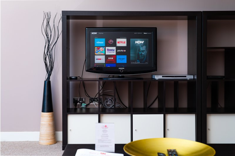Living room with wall-mounted TV, black shelving unit, decorative vase, and yellow cushion