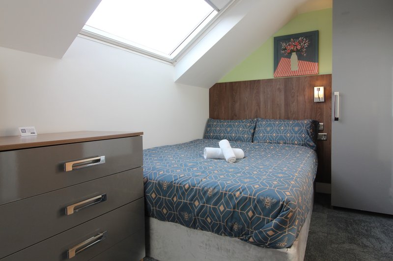 Attic bedroom with double bed, patterned blue bedding, dark wood headboard, chest of drawers, and skylight window