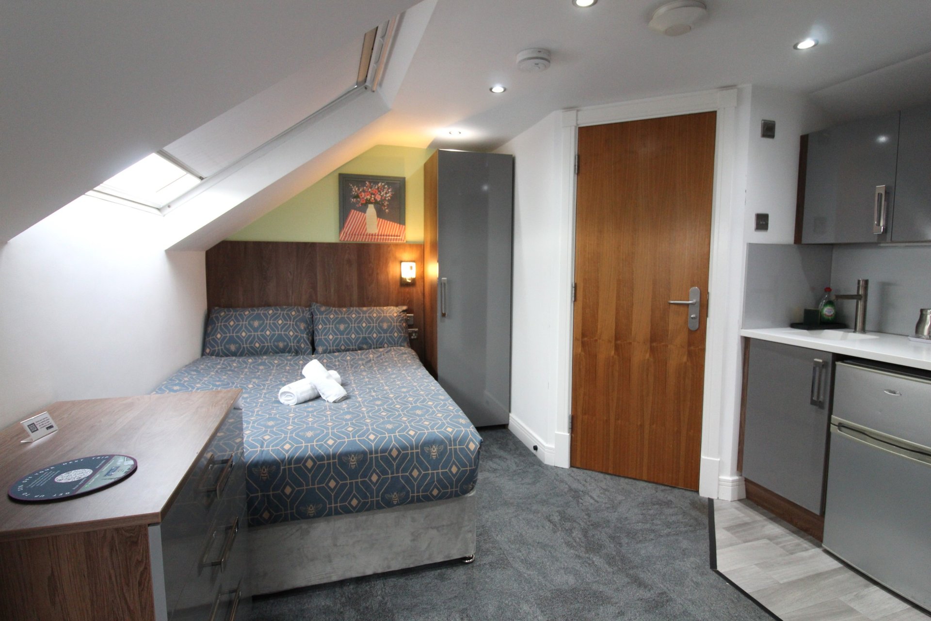 Studio bedroom with double bed, kitchenette, wooden doors and skylight window