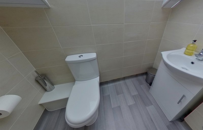 Clean bathroom with toilet, corner sink, tiled walls and vinyl flooring
