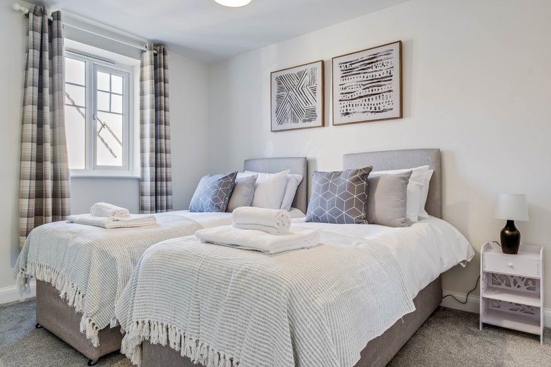 Modern bedroom with two single beds, grey headboard, patterned cushions and white bedding