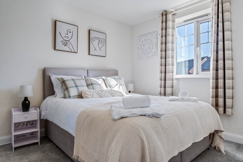 Bright bedroom with grey upholstered bed, white bedside table, framed line art, and checkered curtains