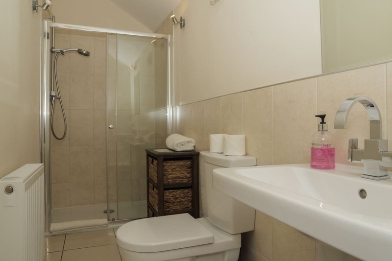 Bathroom with toilet, vanity sink, mirror, shower enclosure and woven storage unit