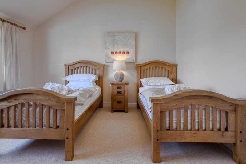 Bright bedroom with four wooden single beds, bedside table, and neutral décor
