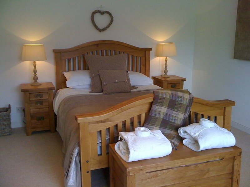 Wooden bedroom with double bed, bedside tables, lamps, and folded towels on bench