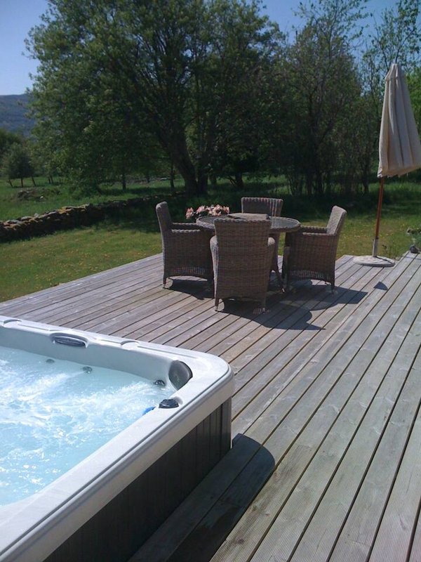 Wooden deck with hot tub, dining table, umbrella and garden views