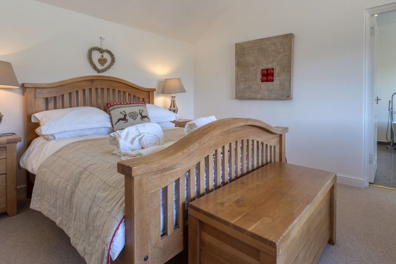 Bedroom with wooden bed frame, neutral bedding, bedside lamps, and wooden bench at foot of bed