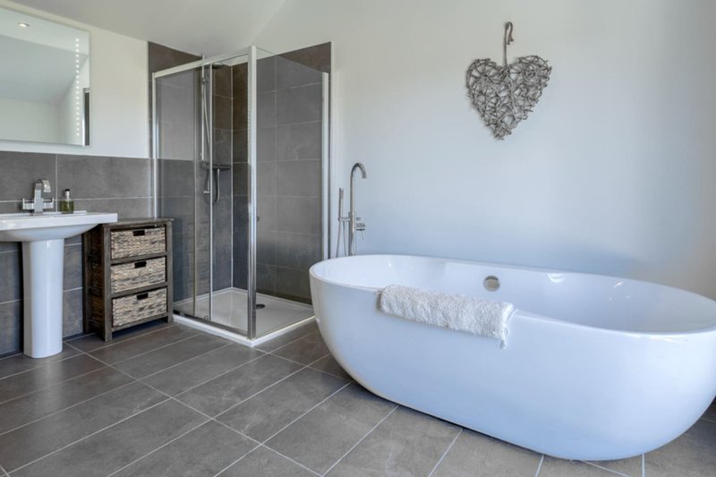 Modern bathroom with freestanding white bathtub, enclosed shower, sink and grey tile flooring
