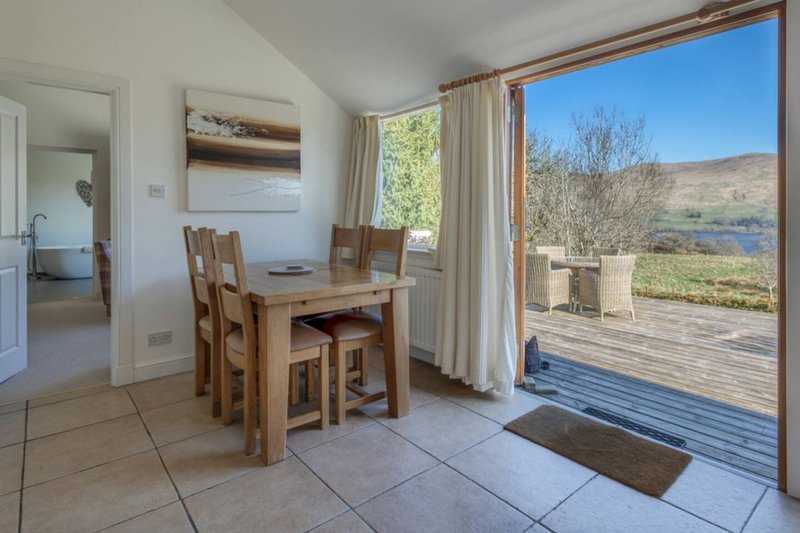 Bright dining area with wooden table and chairs, large windows overlooking garden and countryside views
