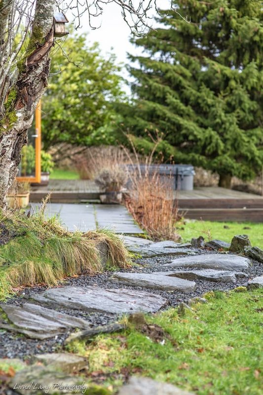 Garden pathway with stepping stones, ornamental grasses, trees and pond in background