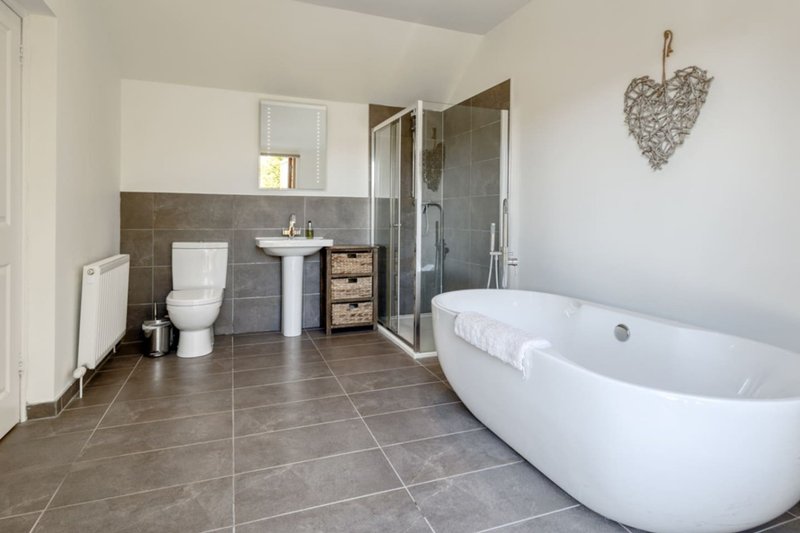 Modern bathroom with freestanding white bath, grey tile flooring, pedestal sink, and shower enclosure
