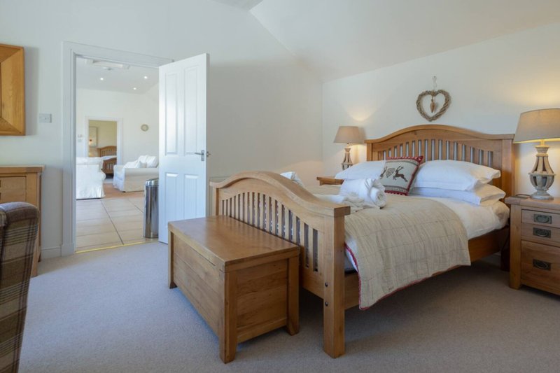 Spacious bedroom with wooden bed frame, two bedside tables, lamps, and en-suite bathroom