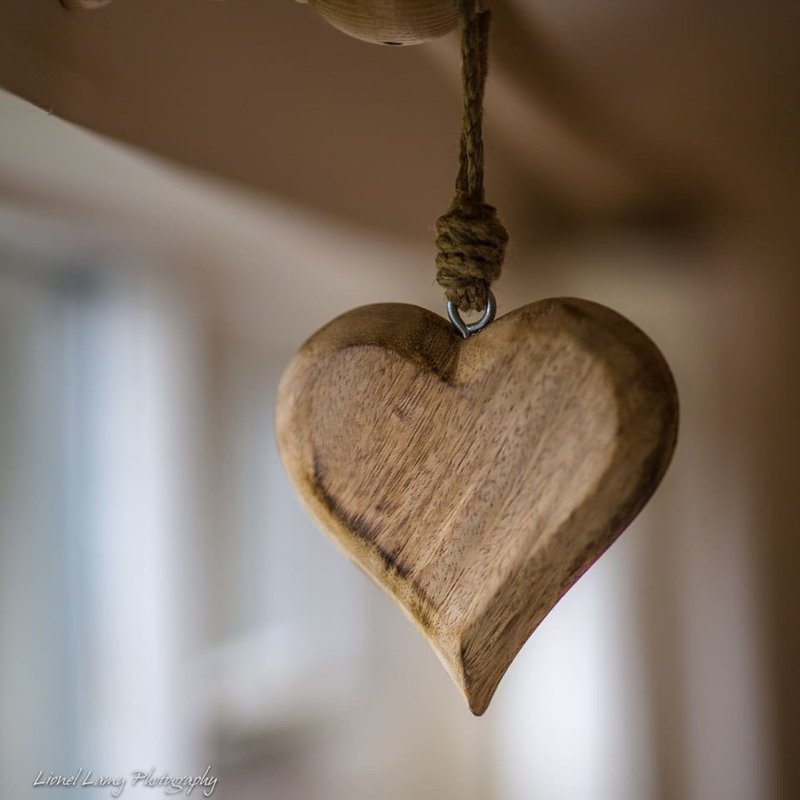 Wooden heart decoration hanging from rope with blurred interior background