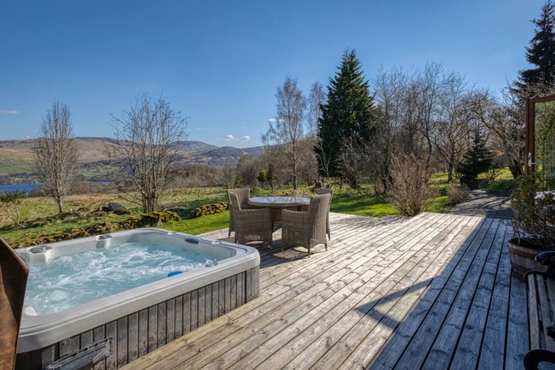 Outdoor deck with hot tub, seating area, and views of lake and mountains