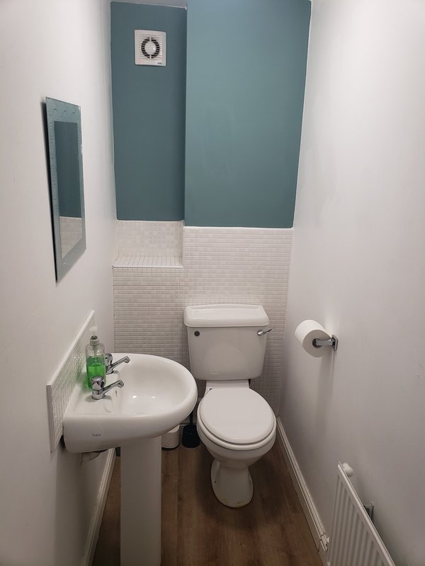 Small bathroom with white pedestal sink, toilet, teal and white tile walls, and wreath decoration