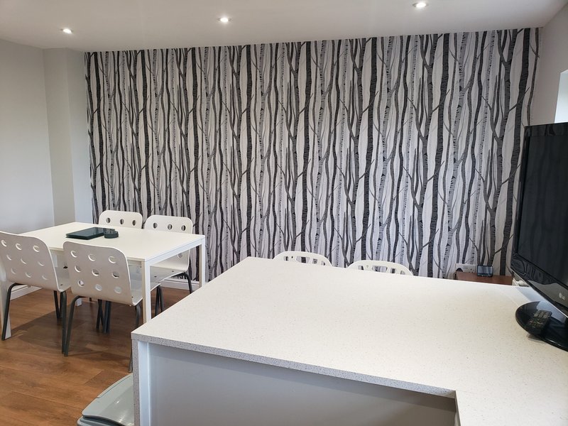Open-plan living space with white desk, dining table, striped curtains and TV