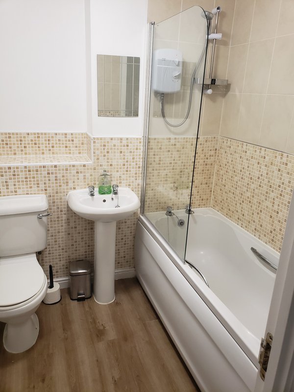 Bathroom with pedestal sink, toilet, bathtub with shower screen and mosaic tile walls