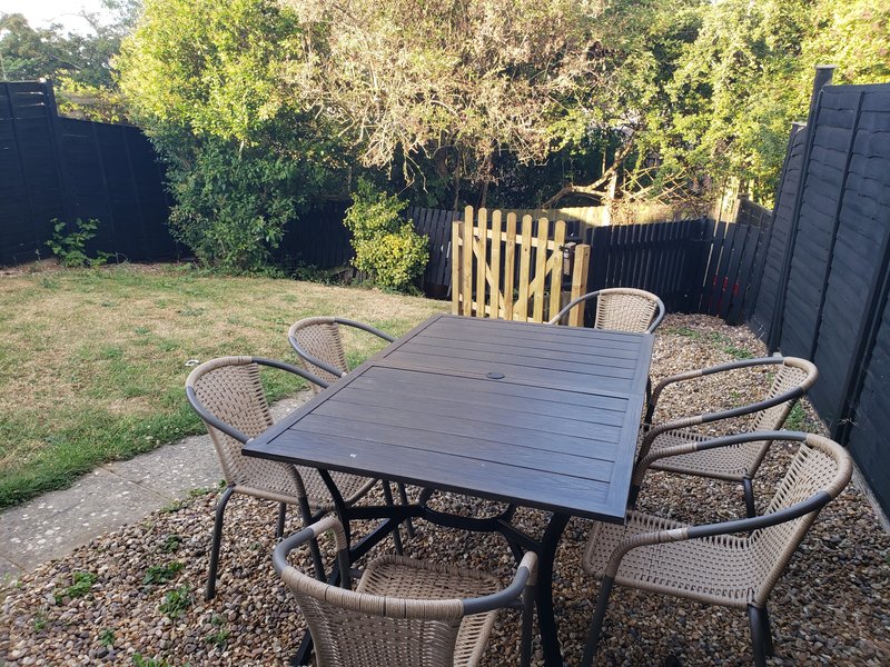Garden patio with dark dining table, woven chairs and wooden fence surrounding lawn