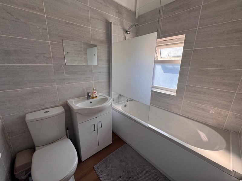 Modern bathroom with toilet, sink vanity, bathtub, and tiled walls with window