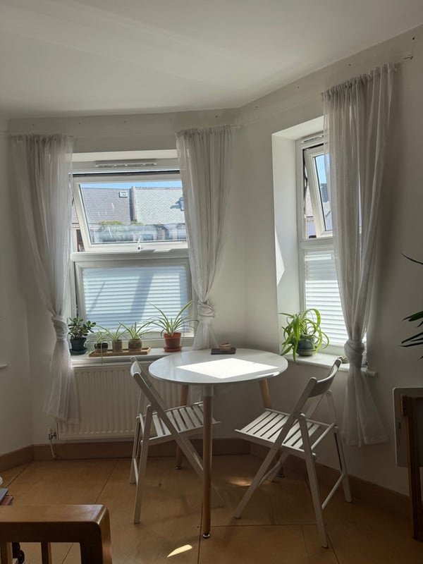 Bright dining nook with white round table, two chairs, large windows and potted plants