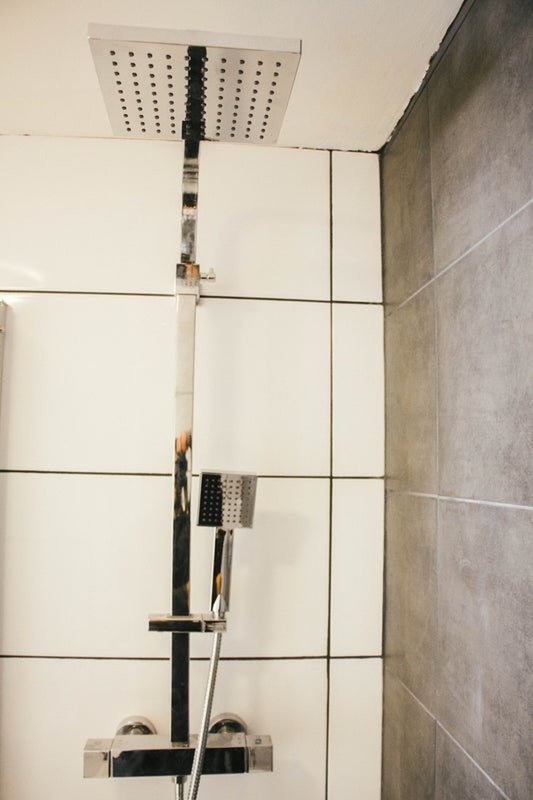 Modern bathroom shower setup with rainfall showerhead, handheld spray, and black fixtures mounted on white tiled wall