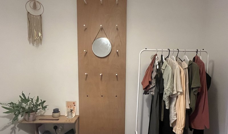 Bedroom with wooden pegboard, round mirror, clothing rack, and potted plant on shelf