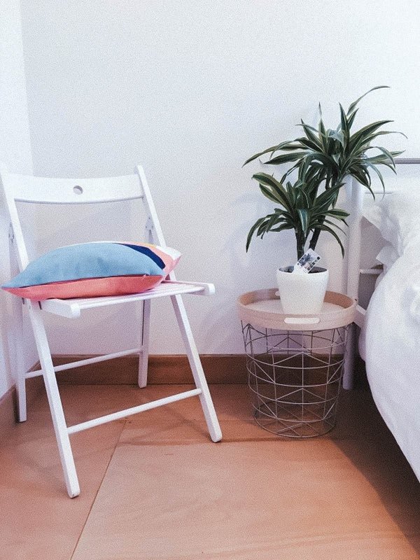 Minimal bedroom corner with white chair, potted plant, and wire basket table