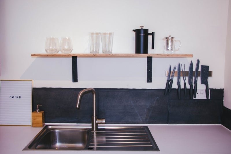 Modern kitchen with sink, wooden shelf, black backsplash and neatly arranged glasses and utensils