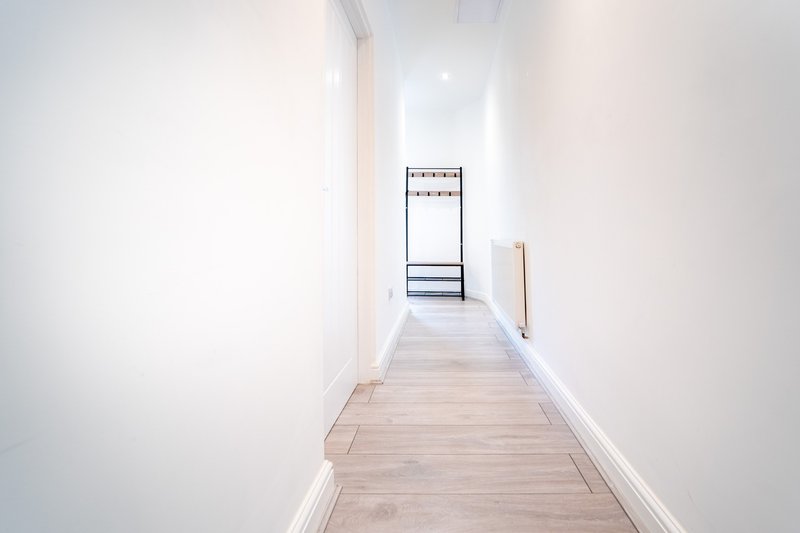 Long narrow hallway with light wood flooring, white walls and metal coat rack at end