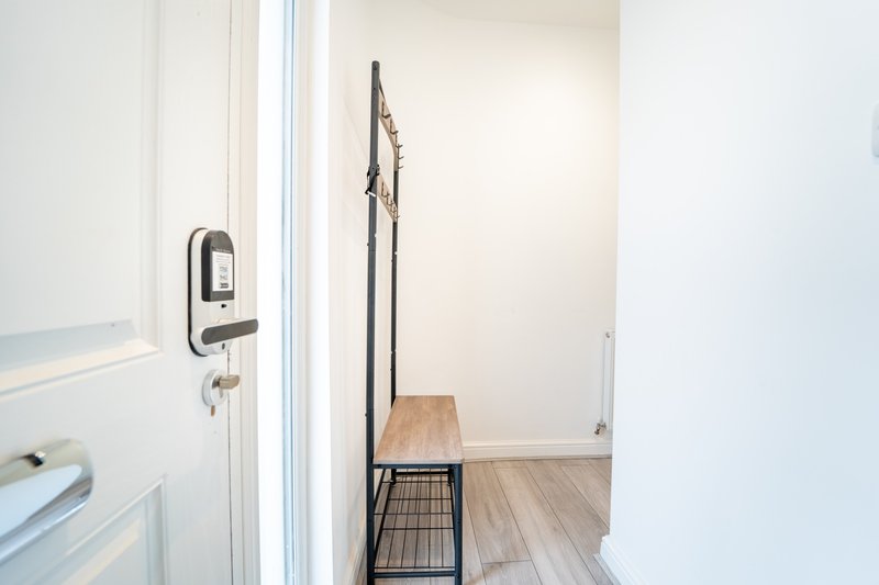 Narrow hallway with white walls, wooden floor, digital door lock, and a bench with storage basket