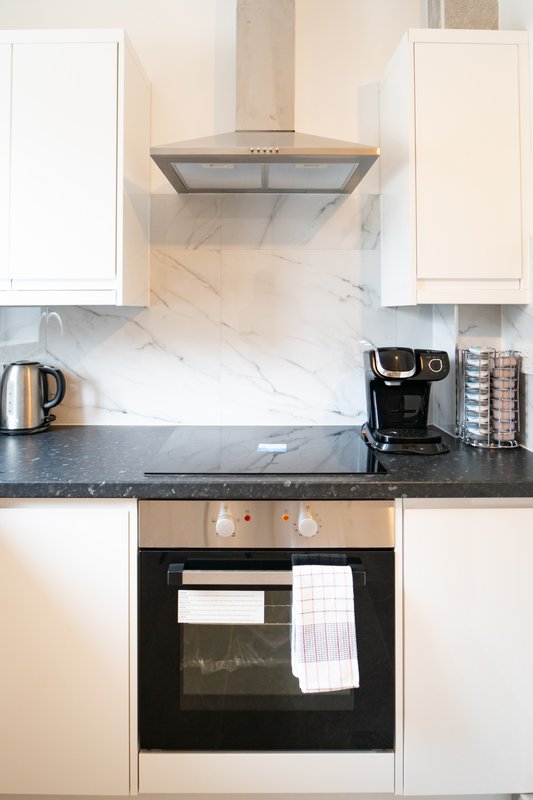 Modern kitchen with white cabinets, marble backsplash, stainless steel range hood, and black countertop