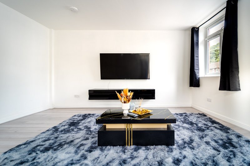 Modern living room with wall-mounted TV, black coffee table, blue rug and window with black curtains