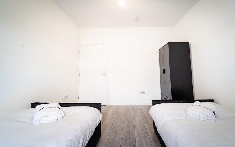 Twin bedroom with two single beds, wooden floor, wardrobe and white walls