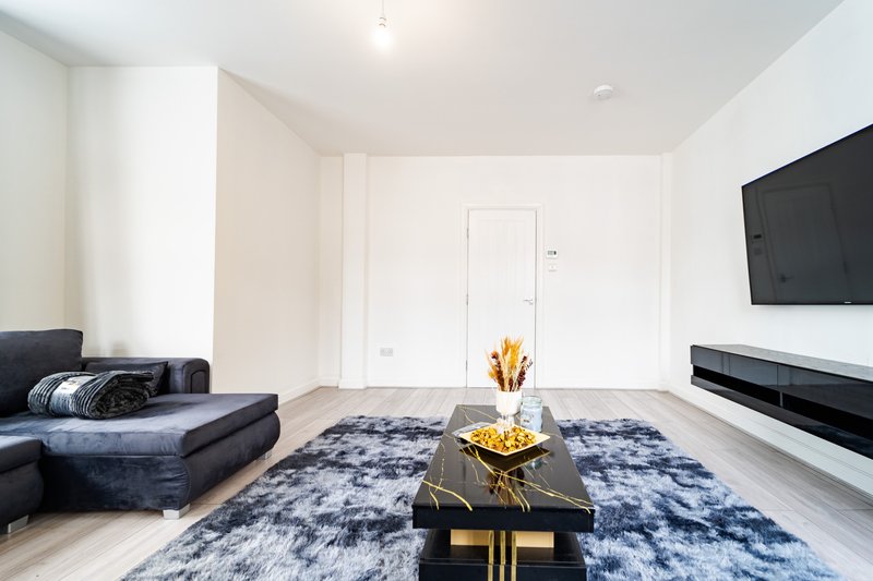Modern living room with dark sofa, blue patterned rug, black coffee table, wall-mounted TV and gold decor accents