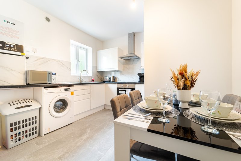 Modern kitchen and dining area with white cabinetry, washing machine, and black dining table set