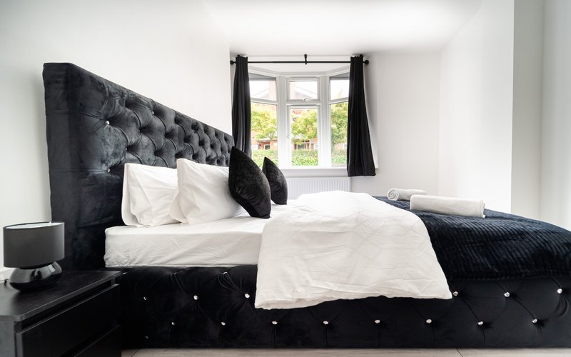Modern bedroom with black upholstered bed, white bedding, and window with natural light