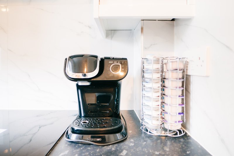 Kitchen counter with coffee maker, glass carafe, and marble backsplash