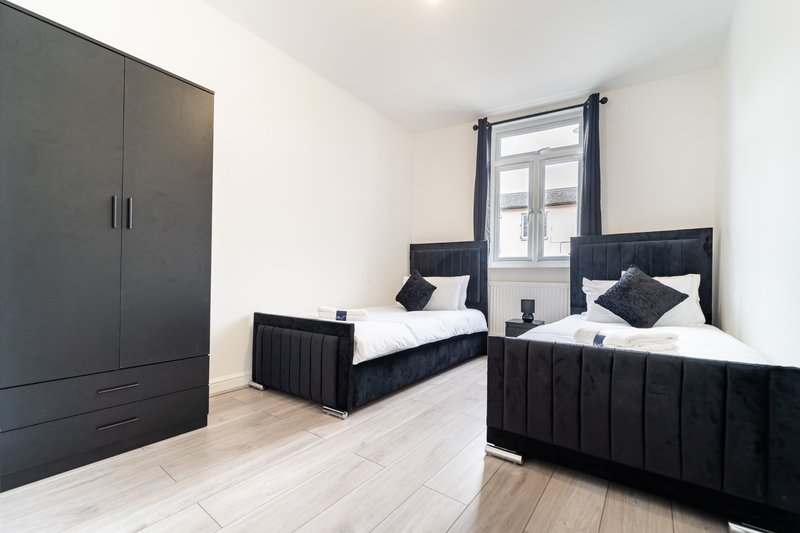 Twin bedroom with two black beds, wardrobe, window with curtains, light wooden floor
