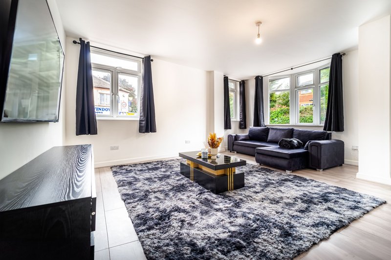Modern living room with black sofa, patterned rug, coffee table, and multiple windows
