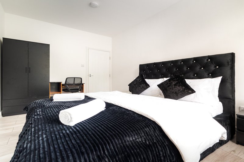 Modern bedroom with black upholstered bed, white pillows, dark bedding, wardrobe and white door