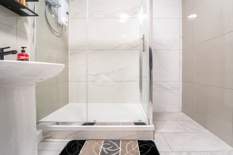 Modern bathroom with marble tiles, glass shower enclosure, pedestal sink and mirror