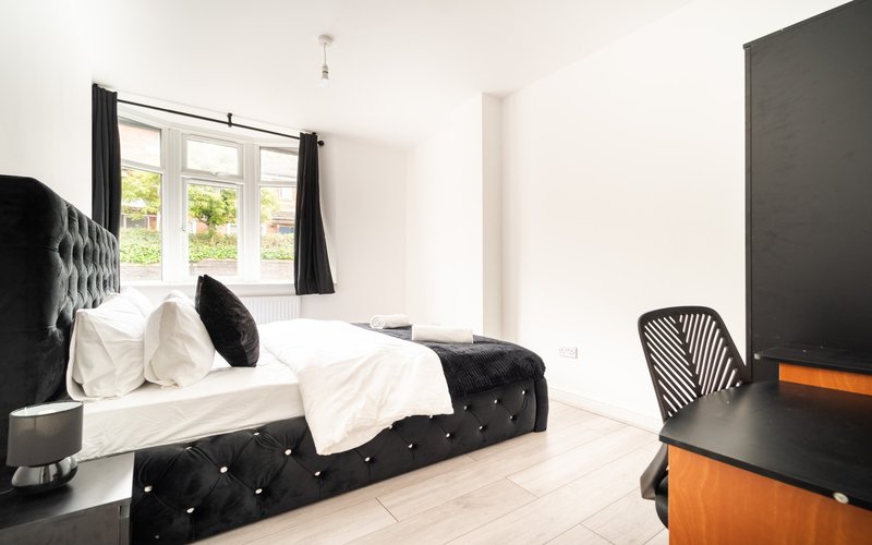 Modern bedroom with black upholstered bed, white bedding, black chair, and garden view