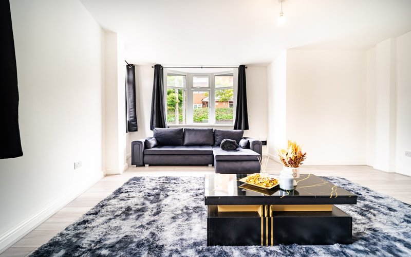 Bright living room with black sectional sofa, patterned rug, and bay window with black curtains